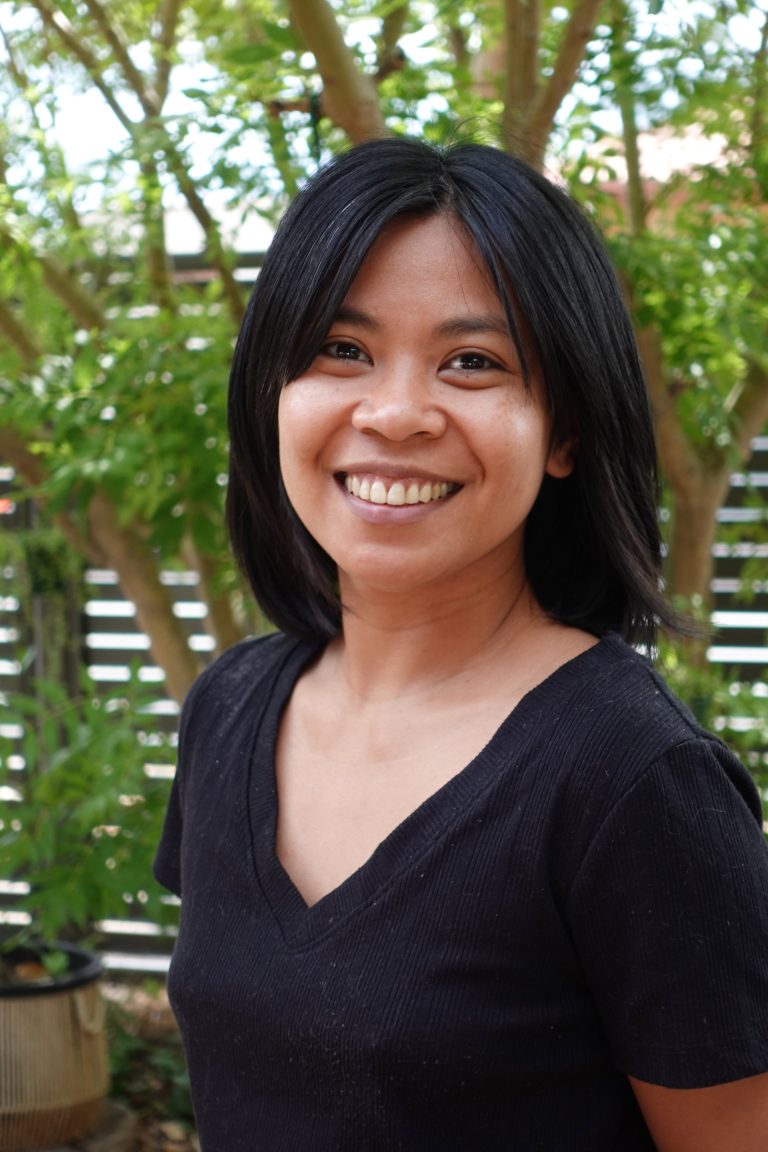 Portrait of Diana Quinones smiling, with green foliage behind her